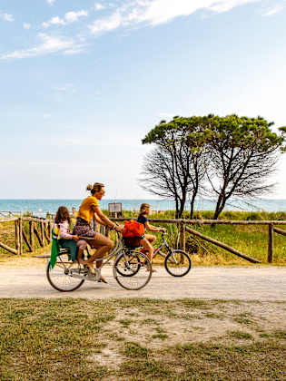 Eine Familie mit zwei Kindern fährt auf Fahrrädern vor den Dünen am Meer entland.