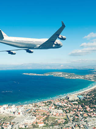 Flugzeug fliegt über eine Küstenstadt an blauem Himmel © iStock.com/jpgfactory