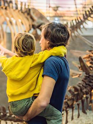 Ein Vater hat ein Kind auf dem Arm und beide schauen auf ein Dinosaurier Skelett