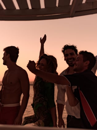 Freunde tanzen bei Sonnenuntergang auf einem Schiff. © BraunS/E+ via Getty Images