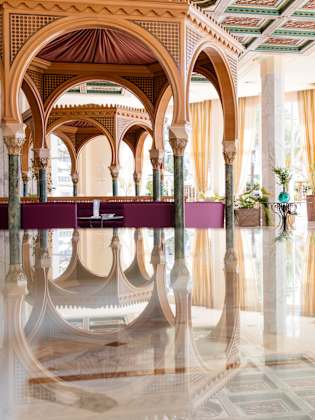 Das Bild zeigt ein modern eingerichtetes Wellnesszentrum. Der Blick geht über eine glatte Wasserfläche auf eine hölzerne Pagode. Die Fenster sind groß und an den Raumwänden stehen Blumen