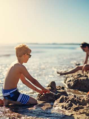 Kinder spielen am Strand und bauen eine Sandburg © iStock.com/Imgorthand
