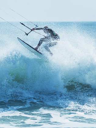 Kitesurfer springt über eine schäumende Welle © iStock.com/shaunl