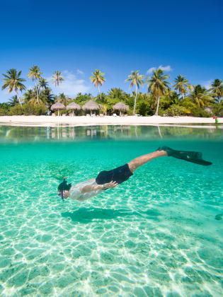 Mann schwimmt unter Wasser mit Insel und Hütten im Hintergrund © iStock.com/shalamov