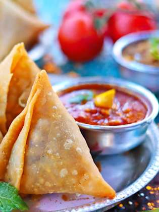 Mehrere Samosas liegen auf einem silbernen Teller mit einer kleinen Soßenschale.