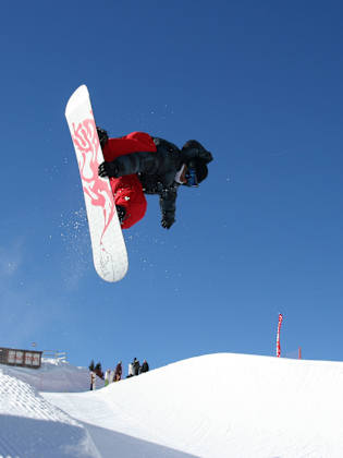 Snowboarder in der Luft beim Trick über einen Kicker im Funpark, blauer Himmel im Hintergrund, Avoriaz, Schweiz.