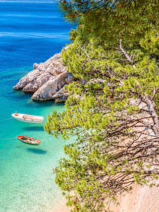 Idyllischer Strand Punta Rata in Brela mit Blick durch mediterrane Bäume, Kroatien. © xbrchx via Getty Images