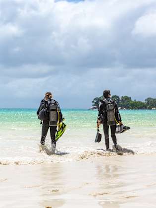 Zwei Taucher mit Ausrüstung laufen am Strand auf ein Boot zu