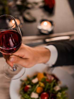 Blick auf zwei Gläser mit Rotwein, mit denen zwei Personen im Restaurant anstoßen