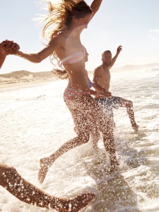 Zwei junge Paare, die am Strand durch das Wasser rennen © iStock.com/pixdeluxe