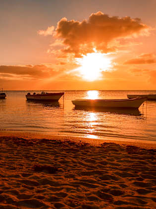 Ein Strand beim Sonnenuntergang mit Booten im Meer