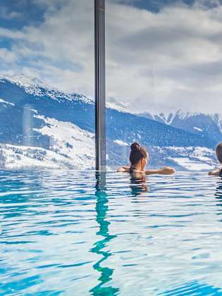 Zwei Frauen in einem Pool blicken auf eine bergige Landschaft