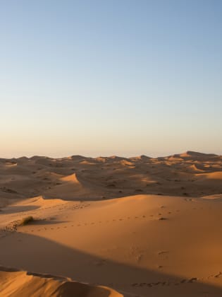 Ein Kind steht mit einem Fernglas auf einer Sanddüne in der Wüste Marokko.