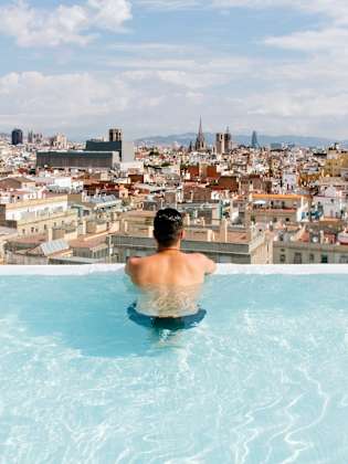Ein Mann schaut aus einem Infinity Pool über Barcelona, Spanien.