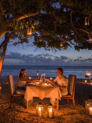 Am Strand von Mauritius, unter einem Baum, sitzt ein Paar, umgeben von Kerzen, an einem Tisch