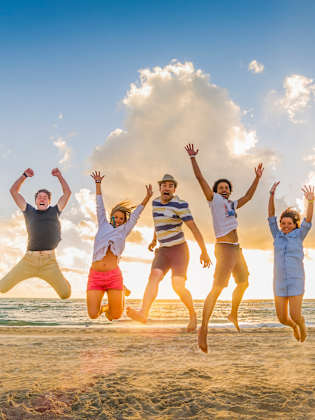 Eine Gruppe von FreundInnen springt an einem Strand in die Luft.