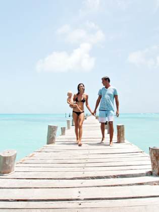 Eltern spazieren mit ihrem Baby auf dem Arm über einen Steg auf dem Meer in Cancún, Mexico.