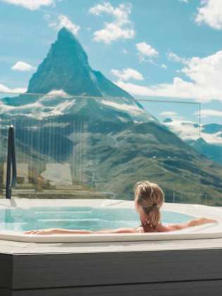 Eine Frau entspannt in einem Whirlpool mit Blick auf die umliegende Berglandschaft.