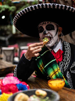 Junger Mann isst und feiert den Tag der Toten in der Bar.