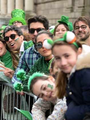 Menschen stehen verkleidet hinter einer Absperrung bei der St. Patrick's Day Parade in Irland.