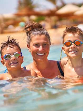 Eine Mutter schwimmt mit ihren beiden Söhnen im Meer und haben Spaß.