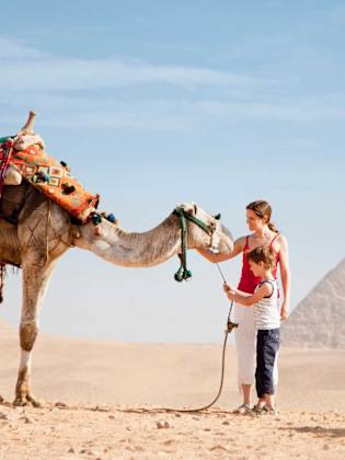 Mutter und Sohn streicheln ein Kamel in der Wüste.