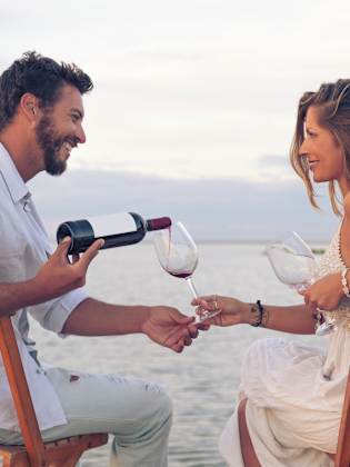 Paar am Strand, Mann gießt Wein in ein Glas ein in Griechenland