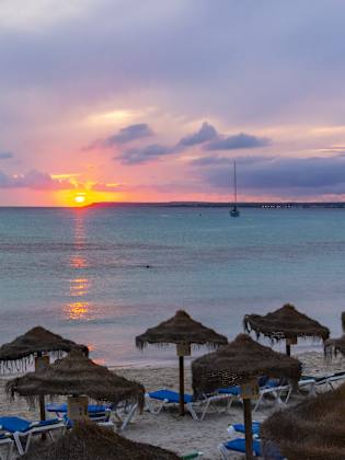 Ein Strand mit Strohsonnenschirmen bei Sonnenuntergang