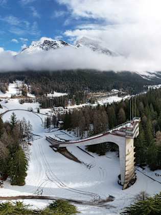 Luftaufnahme mit Blick auf eine alte Sprungschanze in einem bewaldeten Gebiet in den Alpen.