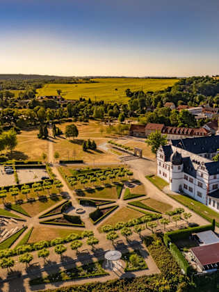 Luftperspektive auf ein Schloss am Rande einer Stadt, welches an einen großen, geometrischen Garten angrenzt.