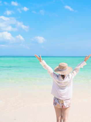 Eine Frau steht mit ausgebreiteten Armen am Meer.