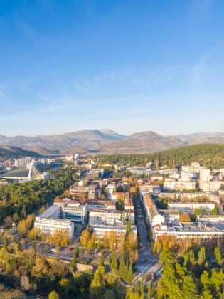 Drohnenausblick über eine Stadtkulisse. Im Hintergrund sieht man eine Bergkulisse.
