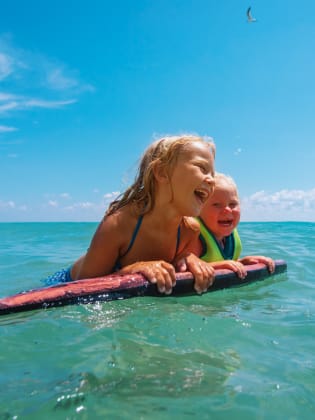 Zwei Kinder schwimmen mit einem Schwimmbrett im Meer.