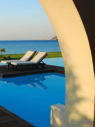 Zwei Sonnenliegen an einem Pool mit Meerblick auf Rhodos, Griechenland.