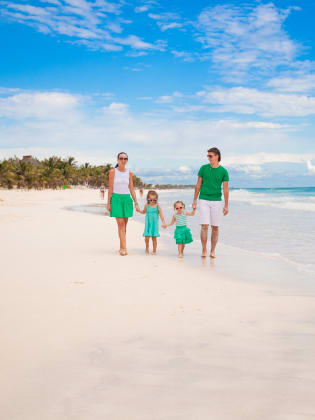 Mutter, Vater und zwei kleine Kinder laufen an einem wunderschönen Strand am Meer entlang.