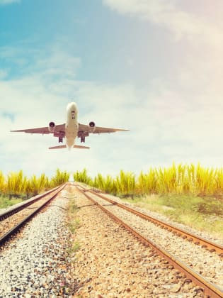 Flugzeug fliegt über Bahnschienen.