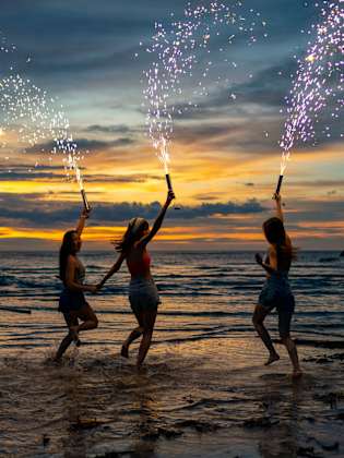 Drei Frauen springen ins Meer mit Silvesterfontänen und haben Spaß