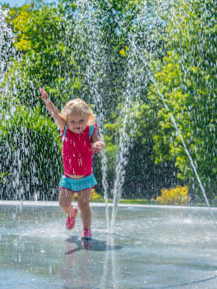 Kleines Mädchen läuft fröhlich durch einen Wasserbrunnen im Sommer.