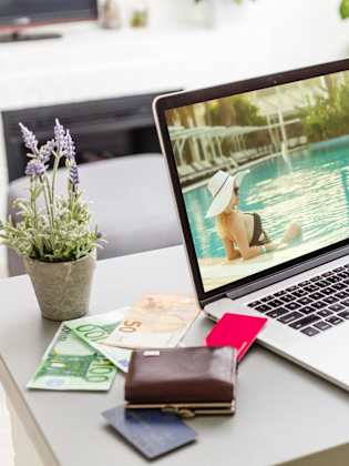 Laptop mit Urlaubsbild, Kamera, Tasche und Bargeld auf einem Tisch.