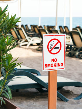 Rauchverbotsschild an einem Strand mit Liegen.