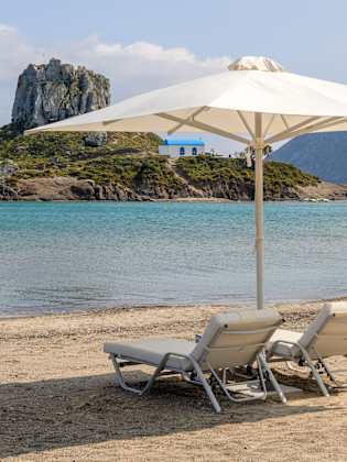Strand Agios Stefanos mit zwei Liegen und Sonnenschirm auf Kos, Griechenland.