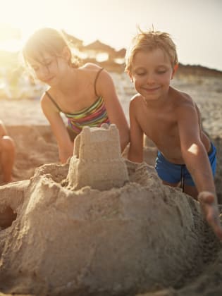 Glückliche Kinder, die eine Sandburg bauen am Strand auf Mallorca, Spanien