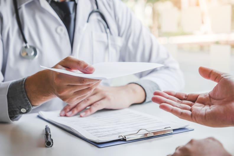 Arzt schreibt eine Diagnose und gibt ein ärztliches Rezept an einen Patienten ©iStock.com/SARINYAPINNGAM