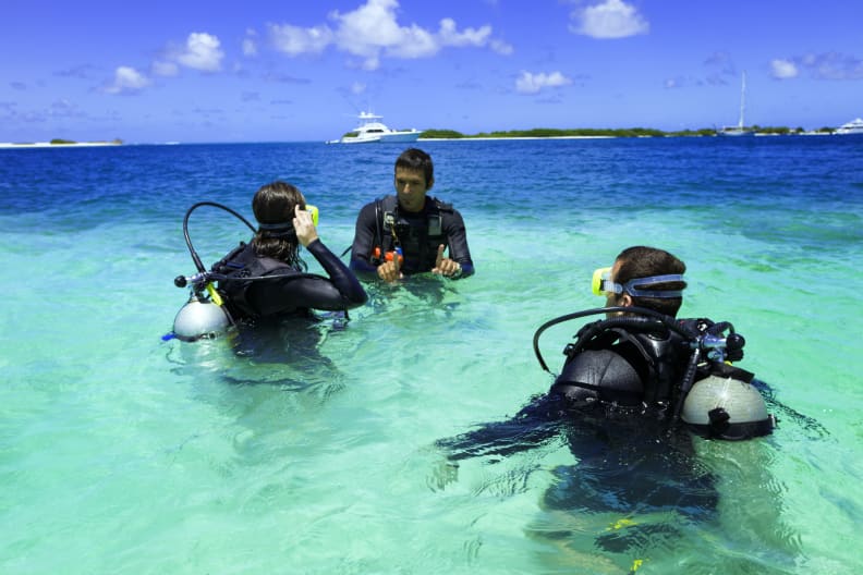 Drei Personen beim Tauchtraining in türkisenem Wasser vor tropischer Insel © iStock.com/apomares