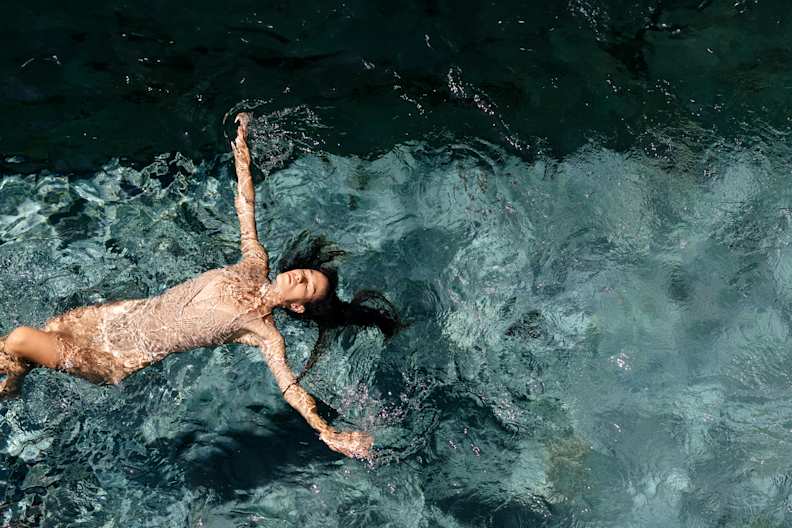 Eine Frau treibt entspannt auf dem Rücken im kristallklaren Wasser, mit geschlossenen Augen und einem Ausdruck purer Gelassenheit.