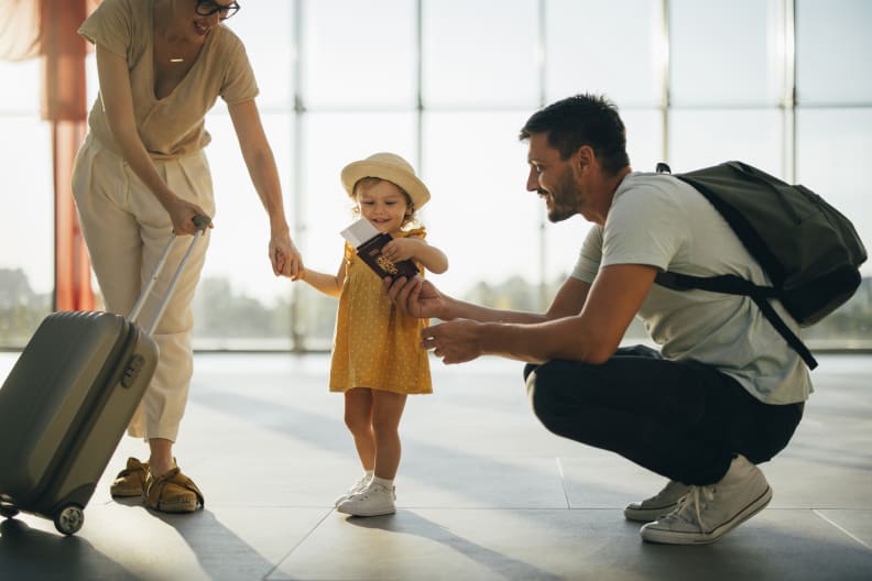 Fröhliche Eltern stehen mit Gepäck und ihrem kleinen Mädchen mit Dokumenten in den Händen am Flughafen ©iStock.com/miniseries