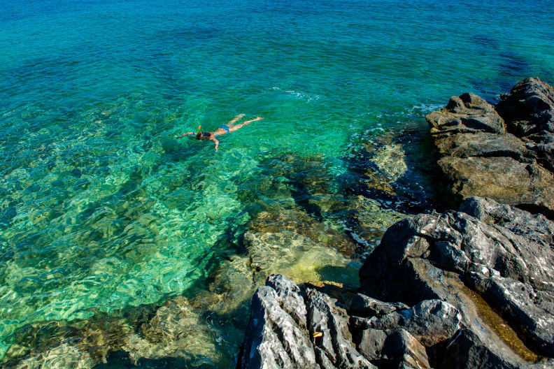 Junges Mädchen schnorchelt durch türkisfarbenes Wasser an der Küste © iStock.com/grafxart8888