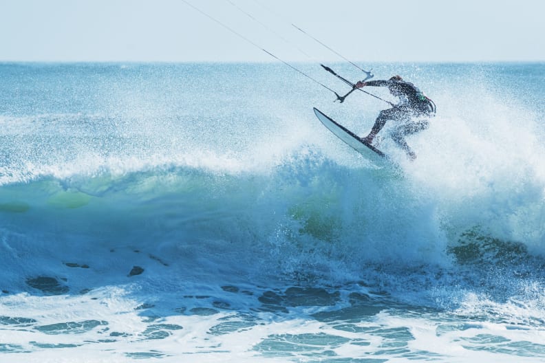 Kitesurfer springt über eine schäumende Welle © iStock.com/shaunl