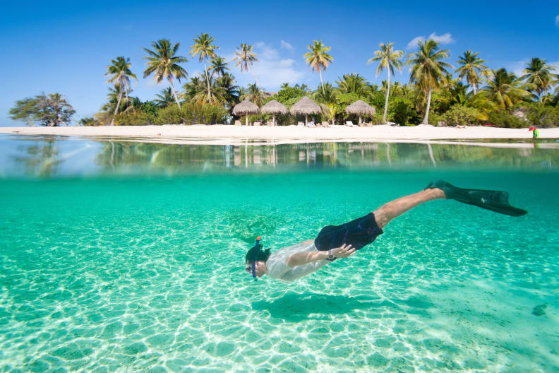 Mann schwimmt unter Wasser mit Insel und Hütten im Hintergrund © iStock.com/shalamov