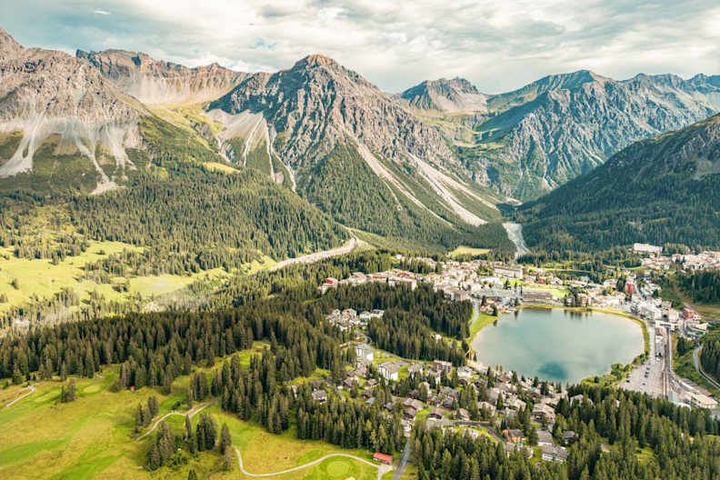 Luftaufnahme des Obersees in Arosa mit umliegendem Bergpanorama, Nadelwäldern und der Ortschaft am Fuße der Graubündner Alpen